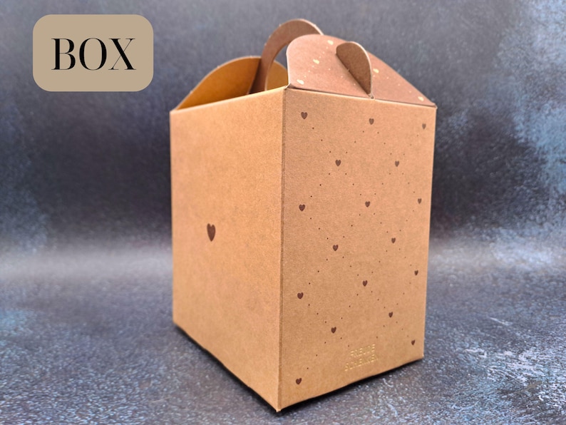 May include: A brown cardboard gift box with a handle and lid, adorned with small heart motifs. The word "BOX" is printed on the top left. Ideal for small gifts or packaging, it has a rustic aesthetic.
