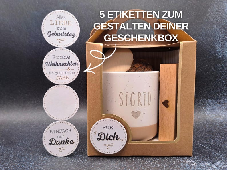 May include: A gift box containing a personalised mug, wooden accent, and decorative items. The mug is white with the name "SIGRID" and a heart. Includes round stickers with phrases like "Happy Birthday" and "Thank You".