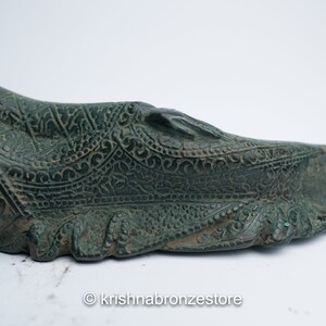 May include: A green bronze reclining Buddha statue with intricate details and a patterned robe. The statue is lying on its side with its head resting on its hand.
