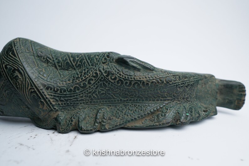 May include: A green bronze reclining Buddha statue with intricate details and a patterned robe. The statue is lying on its side with its head resting on its hand.