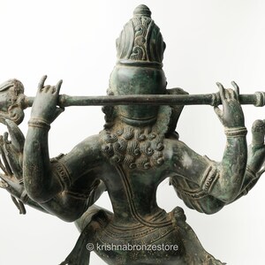 May include: A green bronze statue of a Hindu deity with four arms, holding a flute and a spear. The statue is intricately detailed and has a patina finish.