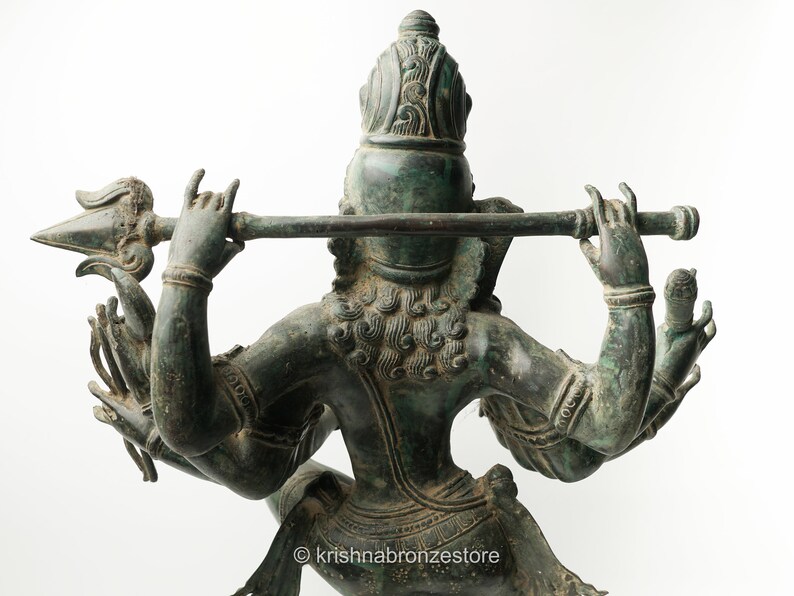 May include: A green bronze statue of a Hindu deity with four arms, holding a flute and a spear. The statue is intricately detailed and has a patina finish.