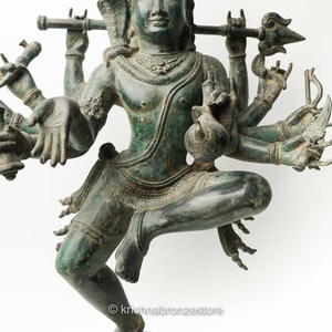 May include: A green bronze statue of a Hindu deity with multiple arms holding various objects. The deity is depicted in a dancing pose with one leg raised.