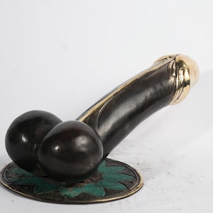 Puede incluir: Una escultura de bronce negro y dorado que representa una anatomía masculina estilizada con una base verde y dorada.