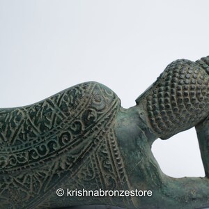 May include: A green bronze reclining Buddha statue with intricate details and a patterned robe. The Buddha's head is resting on the hand, and the statue is lying on its side.