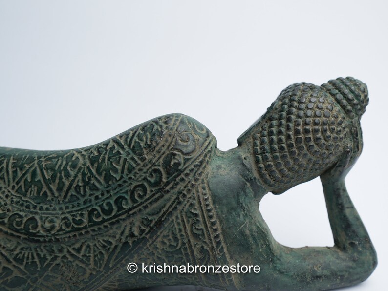 May include: A green bronze reclining Buddha statue with intricate details and a patterned robe. The Buddha's head is resting on the hand, and the statue is lying on its side.