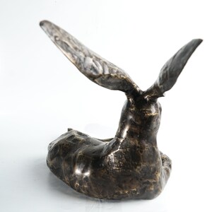K&ouml;nnte beinhalten: Eine Bronzeskulptur eines Hasen mit erhobenen Ohren, der Hase liegt mit dem Kopf zur Seite gedreht.