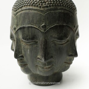 May include: A dark green stone sculpture of a Buddha head with four faces. Each face has closed eyes and a serene expression.