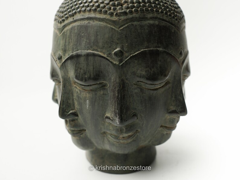 May include: A dark green stone sculpture of a Buddha head with four faces. Each face has closed eyes and a serene expression.