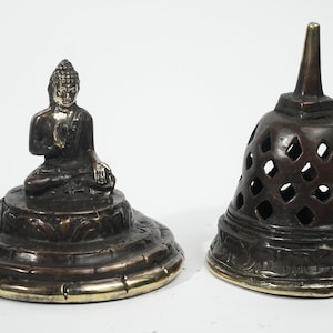 May include: A brass incense burner with a seated Buddha figure on the lid and a decorative, openwork top. The burner has a gold-colored rim.