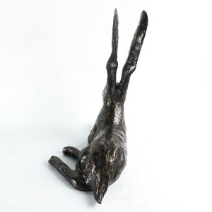 K&ouml;nnte beinhalten: Eine Bronzeskulptur eines Hasen mit hoch erhobenen Ohren. Der Hase liegt auf der Seite mit dem Kopf zur Seite gedreht. Die Skulptur ist detailliert und realistisch.