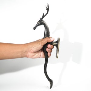May include: A black metal door handle shaped like a deer with antlers. The handle is attached to a brass plate.