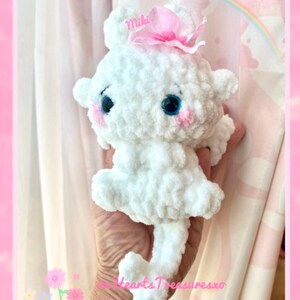 May include: White crocheted plush toy with pink bow and blue eyes. The toy is named "Miki" and is holding a heart-shaped tail.