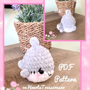 May include: A crocheted gray shark plush toy with pink cheeks and black eyes. The toy is sitting on a wooden surface with a sign that says "PDF Pattern" and "oxHeartsTreasuresxo".