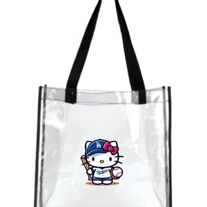 May include: Transparent tote bag with black handles. It features a cartoon Hello Kitty wearing a Dodgers baseball cap and uniform, holding a bat and ball. The Dodgers logo is visible on the cap and uniform.