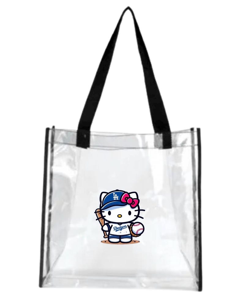 May include: Transparent tote bag with black handles. It features a cartoon Hello Kitty wearing a Dodgers baseball cap and uniform, holding a bat and ball. The Dodgers logo is visible on the cap and uniform.