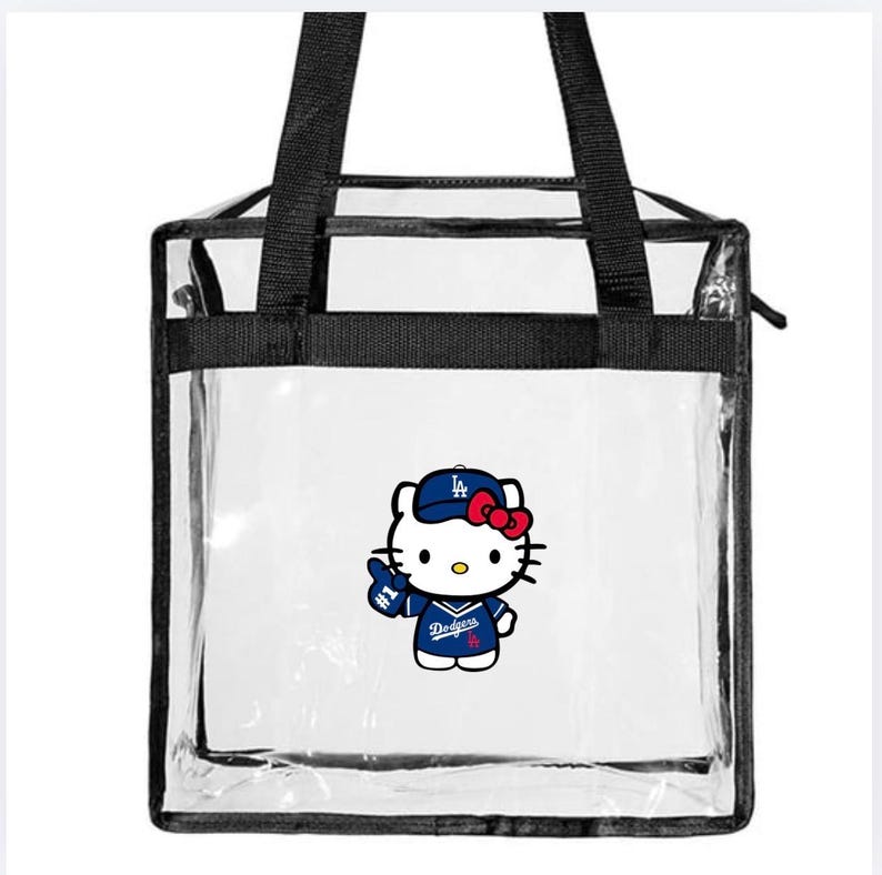 May include: Transparent tote bag with black handles and trim. The bag features a graphic of Hello Kitty wearing a Dodgers baseball uniform and hat. The design includes the Dodgers logo and a red bow.