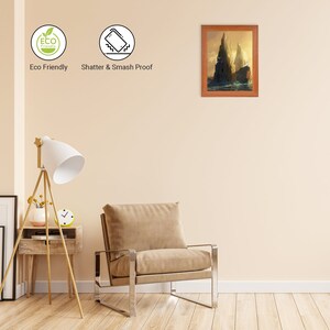 Puede incluir: Una pintura de paisaje enmarcada de dos islas rocosas con un marco de madera. La pintura est&aacute; colgada en una pared beige en un ambiente de sala de estar con un sill&oacute;n marr&oacute;n y una l&aacute;mpara de pie.