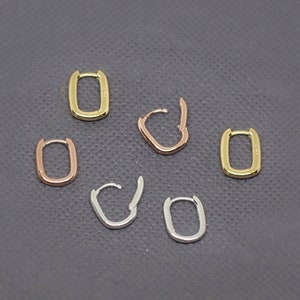 May include: Six small, rectangular hoop earrings in gold, rose gold, and silver tones are arranged on a gray surface. The earrings have a simple, modern design, with a hinged closure.