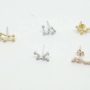 K&ouml;nnte beinhalten: Set aus drei goldenen, silbernen und ros&eacute;goldenen Konstellations-Ohrringen. Jeder Ohrring hat ein zartes Design einer Konstellation mit kleinen funkelnden Steinen.