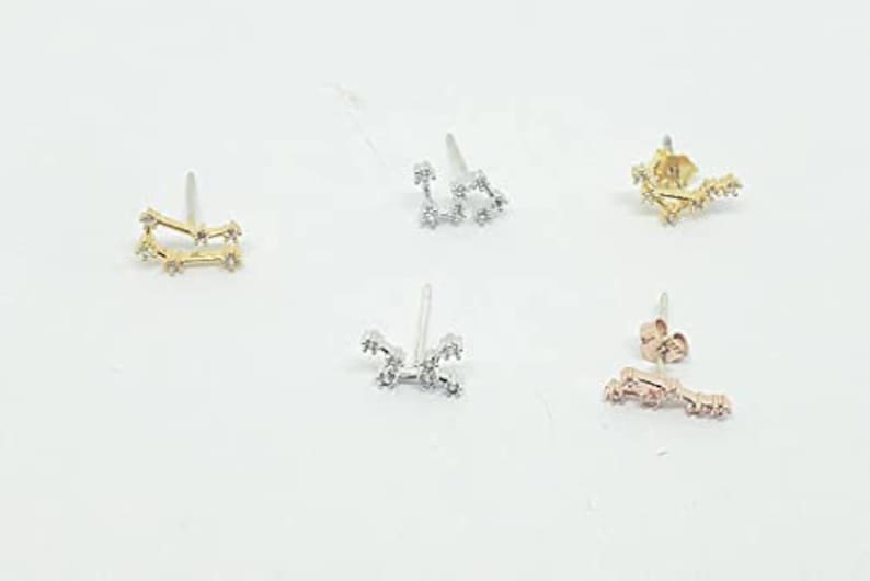 K&ouml;nnte beinhalten: Set aus drei goldenen, silbernen und ros&eacute;goldenen Konstellations-Ohrringen. Jeder Ohrring hat ein zartes Design einer Konstellation mit kleinen funkelnden Steinen.