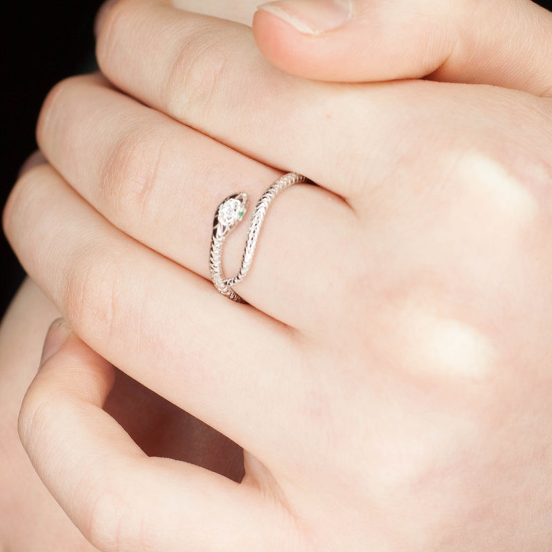 May include: A silver snake ring with a small clear stone on the head. The ring is wrapped around a finger.