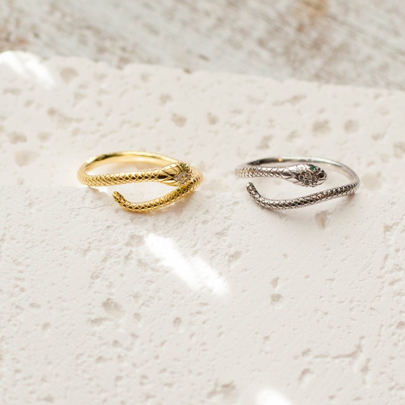 May include: Two snake rings, one gold and one silver, with green stones for eyes. The rings are on a white background.