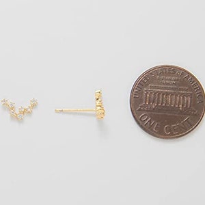 K&ouml;nnte beinhalten: Ein Paar goldene Ohrringe mit einem kleinen Cluster aus klaren Zirkonia-Steinen. Die Ohrringe werden neben einem US-Cent zur Gr&ouml;&szlig;envergleich gezeigt.