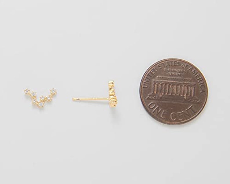 K&ouml;nnte beinhalten: Ein Paar goldene Ohrringe mit einem kleinen Cluster aus klaren Zirkonia-Steinen. Die Ohrringe werden neben einem US-Cent zur Gr&ouml;&szlig;envergleich gezeigt.