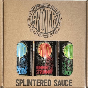 Könnte beinhalten: Ein Karton mit drei kleinen Flaschen scharfer Sauce. Die Flaschen sind mit "Splintered" beschriftet und haben unterschiedliche Designs. Der Karton ist mit "Splintered Sauce" beschriftet.