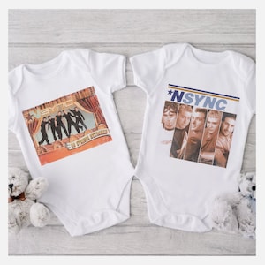 May include: Two white baby onesies with a vintage *NSYNC design. One onesie features a photo of the band with the text "No Strings Attached" and the other onesie features a photo of the band with the text "*NSYNC".