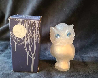 May include: A frosted glass owl figurine with blue eyes and a box with a moon and tree design. The owl is a decorative item, possibly a collectible or a piece of home decor.