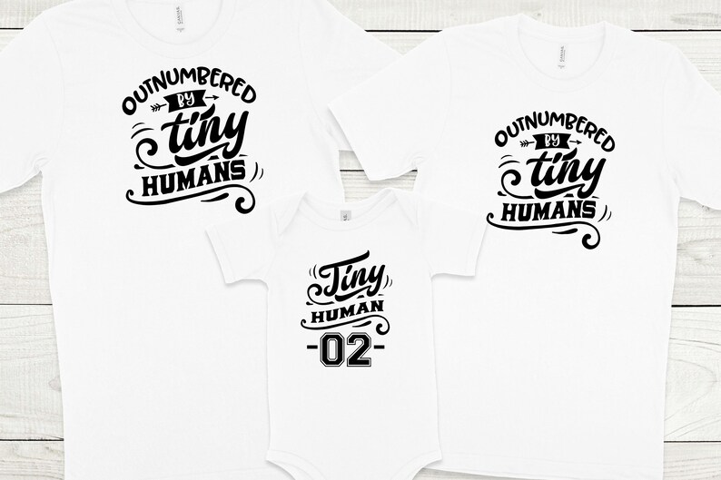 May include: Three white t-shirts with black text. The largest shirt says "Outnumbered by tiny humans". The medium shirt says "Outnumbered by tiny humans". The smallest shirt says "Tiny human -02-"
