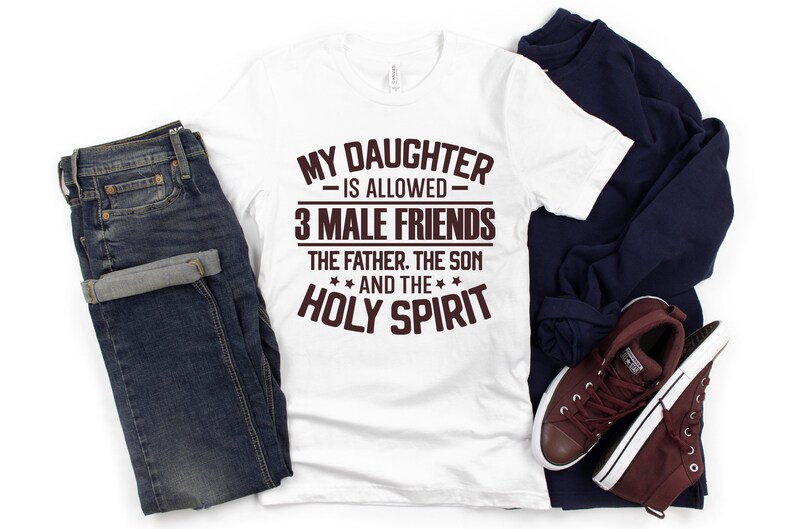 K&ouml;nnte beinhalten: Wei&szlig;es T-Shirt mit dem Text "MY DAUGHTER IS ALLOWED 3 MALE FRIENDS THE FATHER. THE SON AND THE HOLY SPIRIT" in braunen Buchstaben. Das Shirt wird mit blauen Jeans, einem marineblauen Sweatshirt und weinroten Sneakers kombiniert.