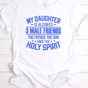 K&ouml;nnte beinhalten: Wei&szlig;es T-Shirt mit blauem Text. Der Text lautet: &bdquo;MEINE TOCHTER DARF 3 M&Auml;NNLICHE FREUNDE HABEN: DER VATER, DER SOHN UND DER HEILIGE GEIST.&ldquo; Das Shirt besteht aus einem weichen Material und hat kurze &Auml;rmel.