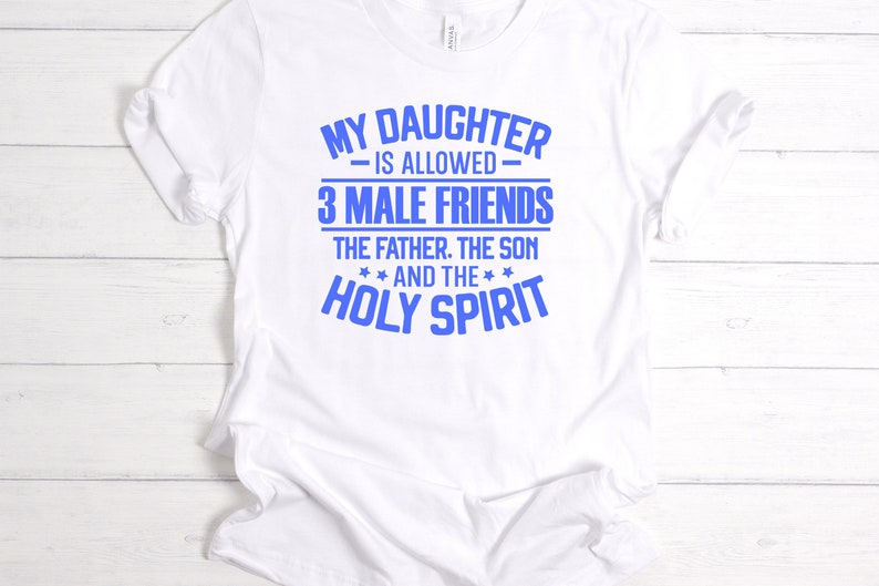 K&ouml;nnte beinhalten: Wei&szlig;es T-Shirt mit blauem Text. Der Text lautet: &bdquo;MEINE TOCHTER DARF 3 M&Auml;NNLICHE FREUNDE HABEN: DER VATER, DER SOHN UND DER HEILIGE GEIST.&ldquo; Das Shirt besteht aus einem weichen Material und hat kurze &Auml;rmel.