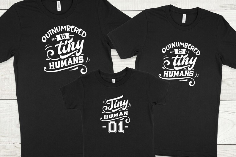 May include: Three black t-shirts with white text. The two larger shirts say "Outnumbered by tiny humans". The smaller shirt says "Tiny human -01-"