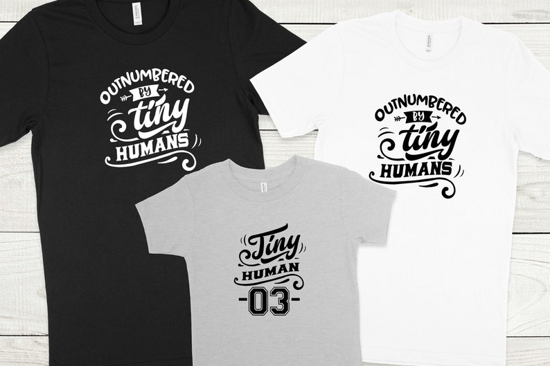 May include: Three t-shirts with a family theme. One black t-shirt says "Outnumbered by tiny humans". One white t-shirt says "Outnumbered by tiny humans". One gray t-shirt says "Tiny human -03".