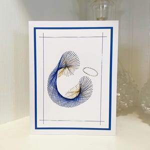 May include: A white card with a blue border, featuring a blue and gold thread art design of a halo and a figure. The design is reminiscent of a religious icon.