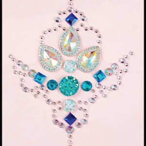 May include: A decorative design made of rhinestones and jewels in shades of blue and turquoise. The design is in the shape of a stylized flower with a teardrop shape in the center. The design is on a pink background.