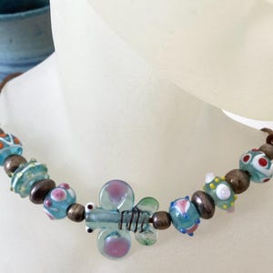 May include: A light blue glass butterfly charm necklace with brown leather cord and colorful glass beads.