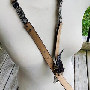 May include: A vintage belt with a silver-tone metal chain and a brown leather strap. The belt features rectangular metal links and a brown leather buckle. The belt is displayed on a mannequin.