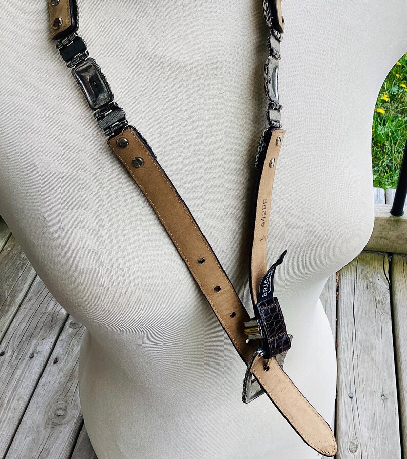 May include: A vintage belt with a silver-tone metal chain and a brown leather strap. The belt features rectangular metal links and a brown leather buckle. The belt is displayed on a mannequin.
