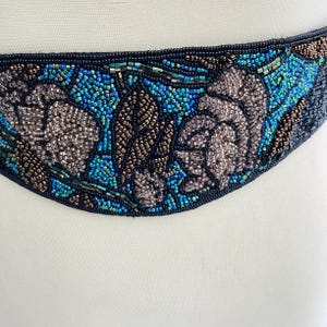 May include: A curved beaded belt, featuring a black base adorned with floral patterns in blue, teal, and brown. The small beads are closely arranged, giving a textured appearance. This belt is likely designed to be worn around the waist, adding a decorative element.