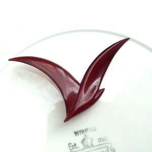 May include: A dark red plastic brooch in the shape of a bird in flight.
