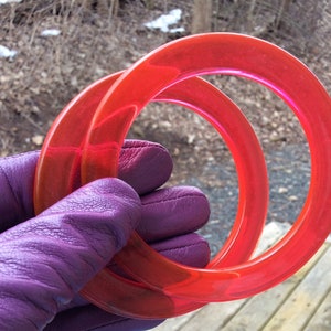 May include: Two bright orange plastic bangles, one slightly larger than the other, held in a purple leather glove.