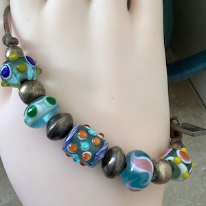 May include: A multi-colored glass bead bracelet with silver beads and a leather cord. The beads are blue, green, yellow, orange, and white with various patterns.