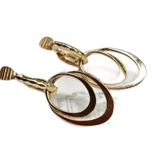 May include: A pair of gold clip-on earrings with a double oval design. The earrings are made of a smooth, shiny metal.