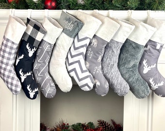 Peut inclure: Ensemble de huit chaussettes de Noël grises et blanches avec différents motifs, notamment du plaid, du chevron et des animaux de la forêt. Les chaussettes sont accrochées à une cheminée blanche.