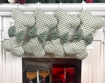 May include: Four Christmas stockings with a green and white gingham pattern and a green polka dot bow. The stockings are hanging above a fireplace decorated with Christmas ornaments and greenery.